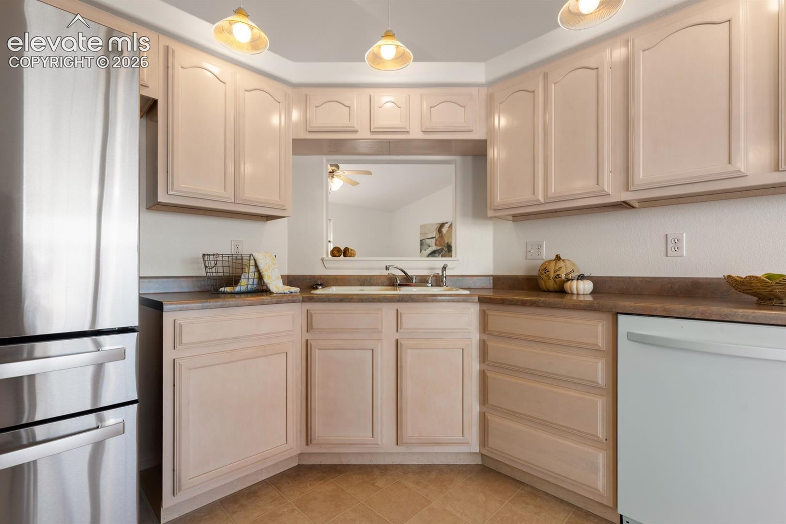Kitchen featuring light-toned cabinetry, laminate countertops, stainless steel refrigerator, white dishwasher, and three pendant lights