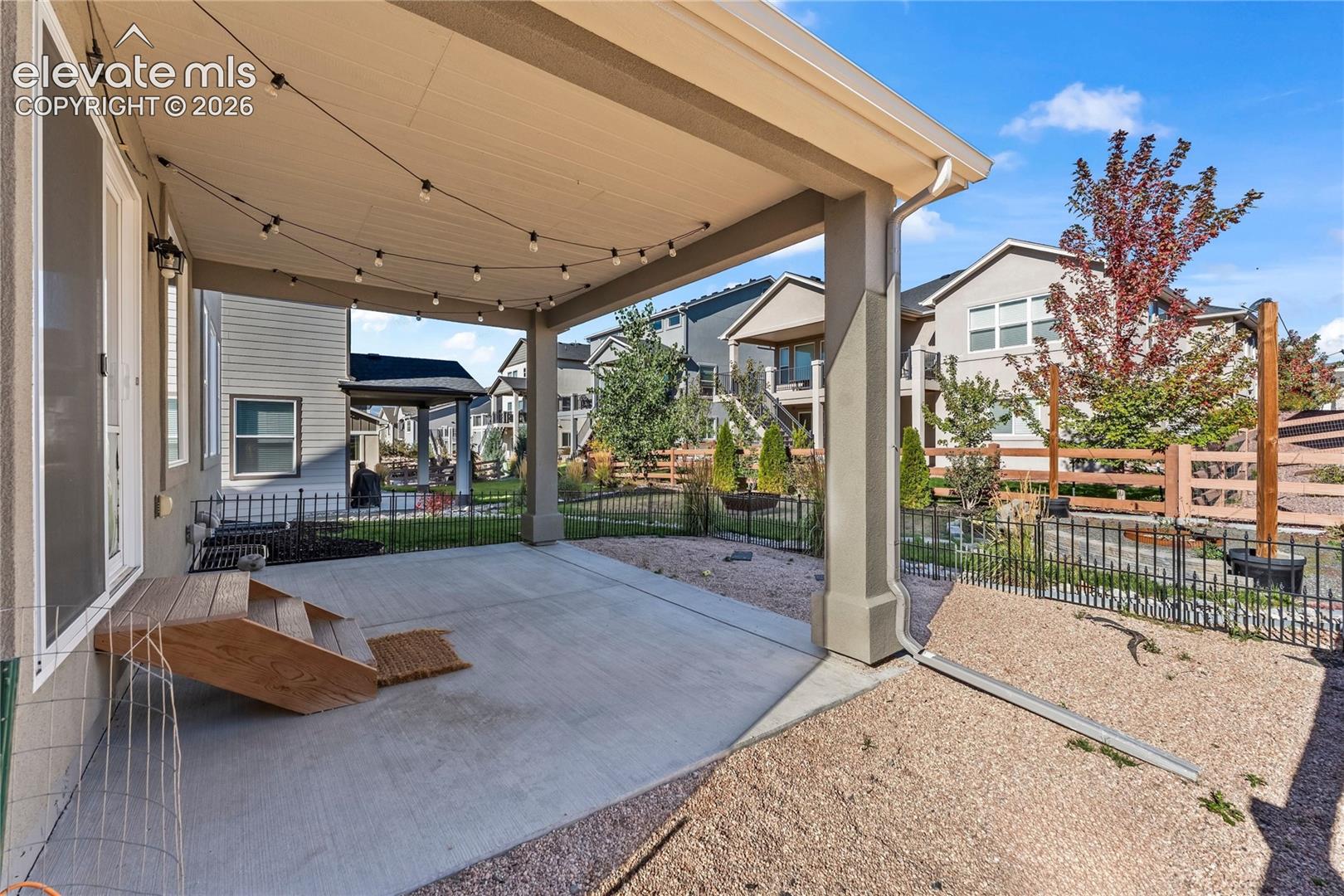 Covered concrete patio featuring a ceiling with integrated light fixtures, low-profile decorative metal fencing, and stone landscape ground cover