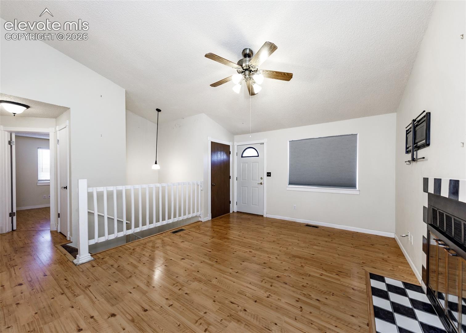 Living area featuring wood-finish flooring, vaulted ceilings, a fireplace with decorative tile surround, a ceiling fan with light kit, and a white picket-style stair railing