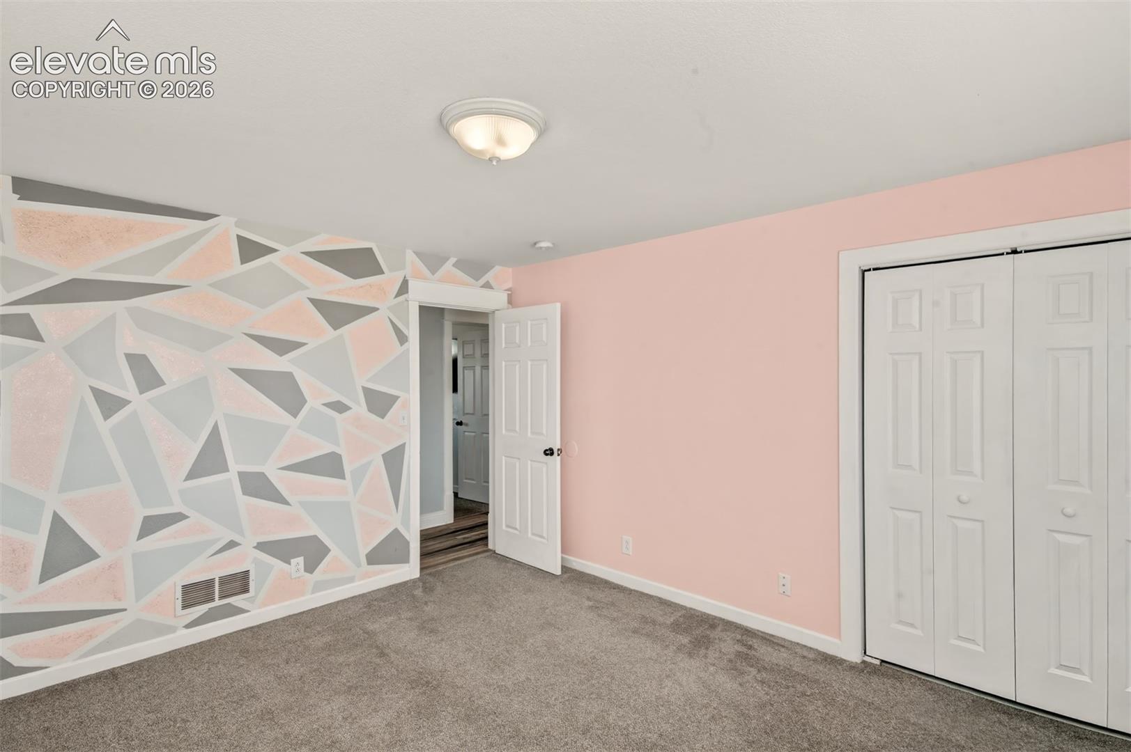 Geometric accent wall, wall-to-wall carpeting, flush-mount ceiling lighting, and double-panel closet doors