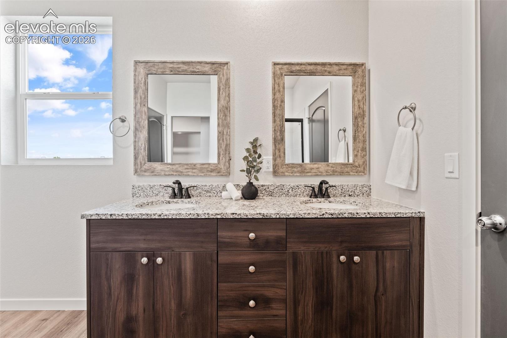 Double vanity with granite countertop, wood-finish cabinetry, dual sinks, and individual framed mirrors