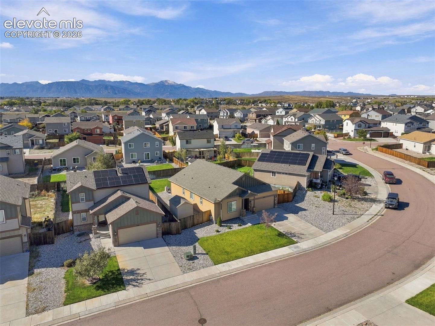 Aerial view featuring residential properties with asphalt-shingle roofs, solar panel installations, concrete driveways, and mountain scenery