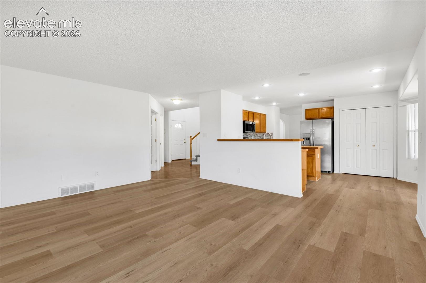 Open-concept living space featuring wood-finish flooring, white walls, recessed lighting, and a partial wall separating the kitchen area