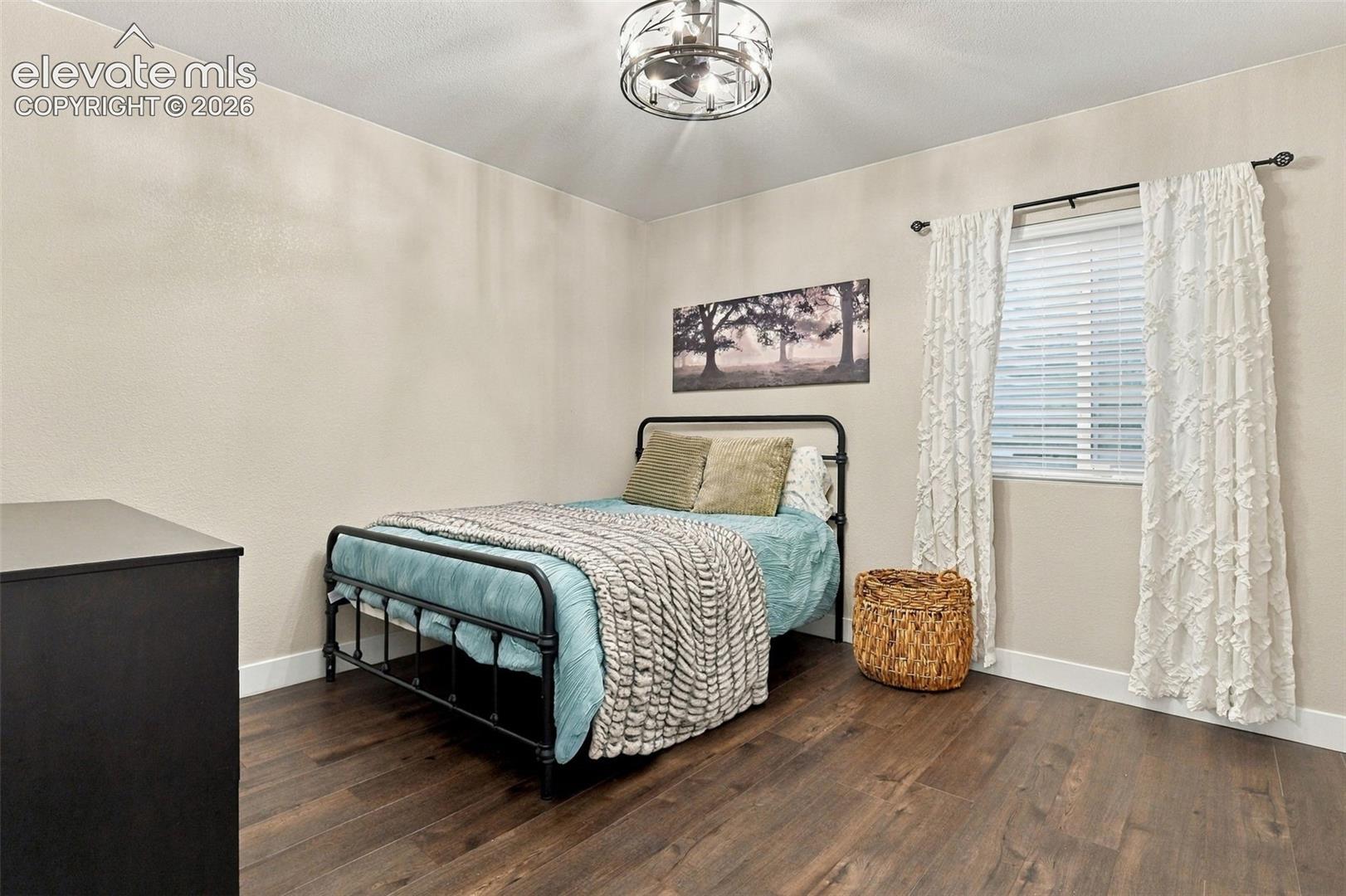 Room featuring dark wood-finish flooring, a drum-style chandelier with a metal cage frame, and a window equipped with horizontal blinds
