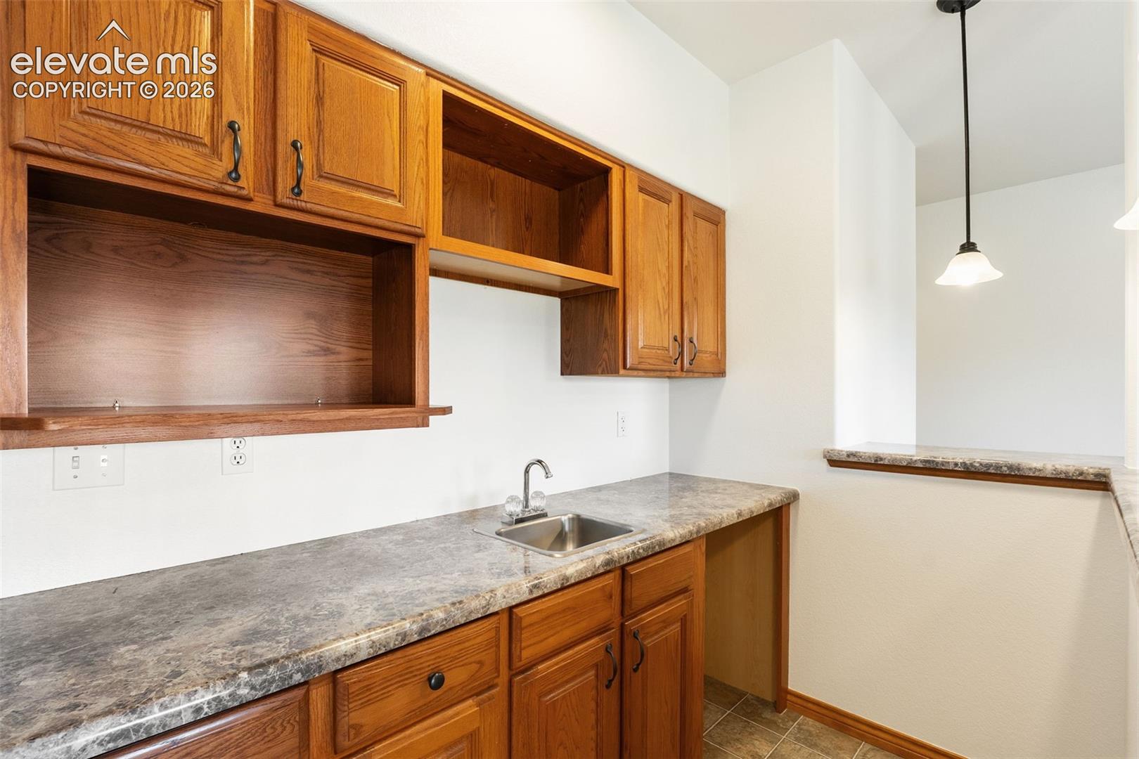 Built-in wood cabinetry, stone-patterned laminate countertop, stainless steel drop-in sink, pendant lighting, and tile flooring