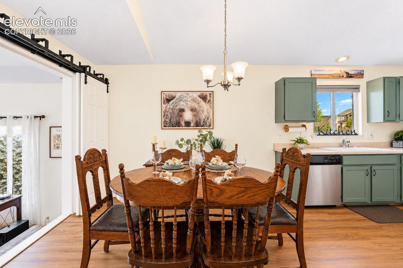 Dining area featuring wood-finish flooring, a three-light chandelier, and black sliding barn door hardware