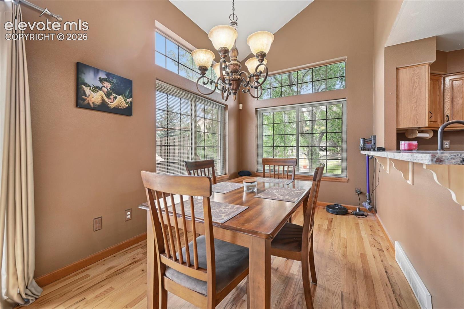 Vaulted ceiling, wood-finish flooring, large picture windows, transom windows, and an ornate chandelier