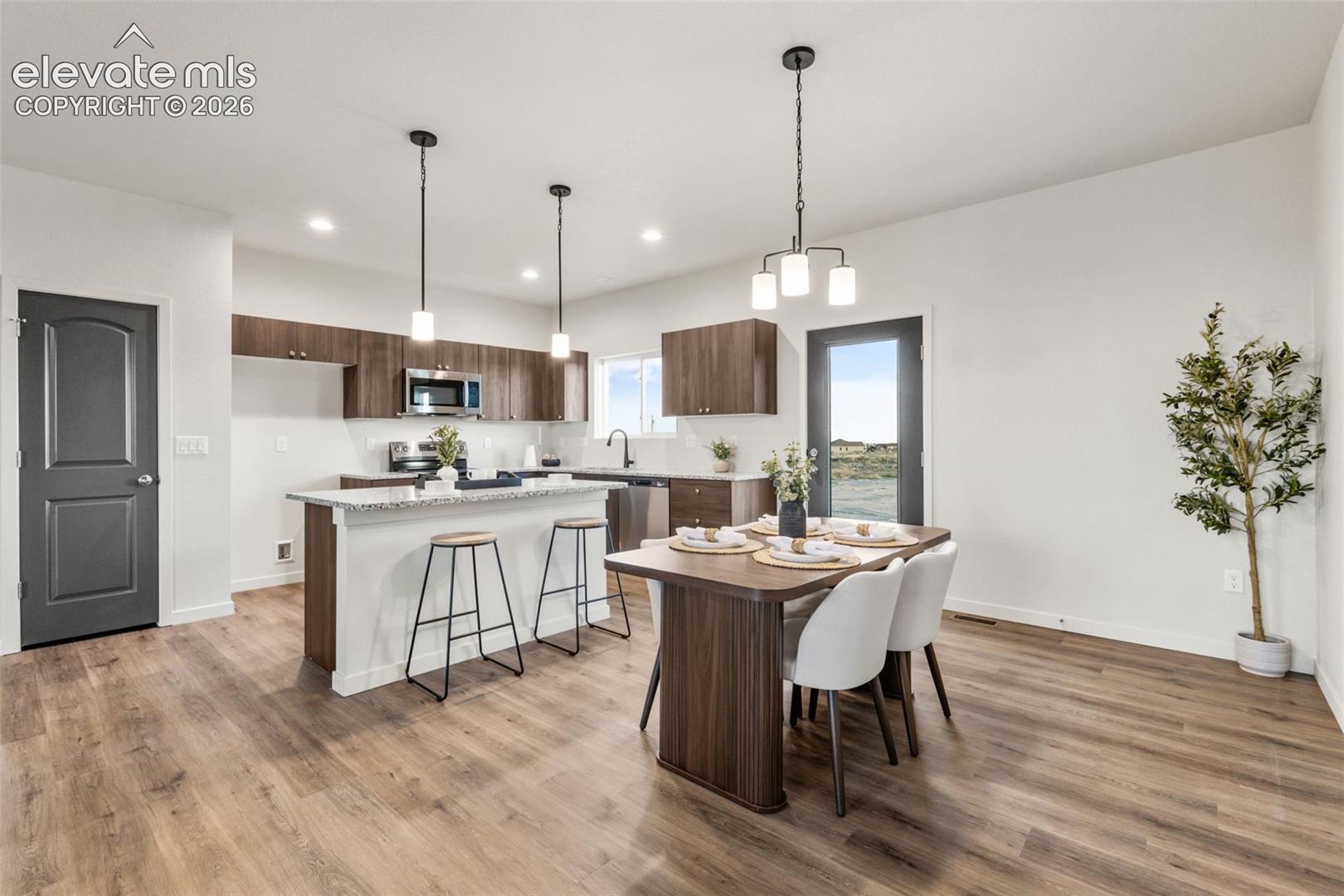 Kitchen featuring wood-finish cabinetry, an island with stone-finish countertops, stainless steel appliances, wood-finish flooring, and multi-light pendant fixtures