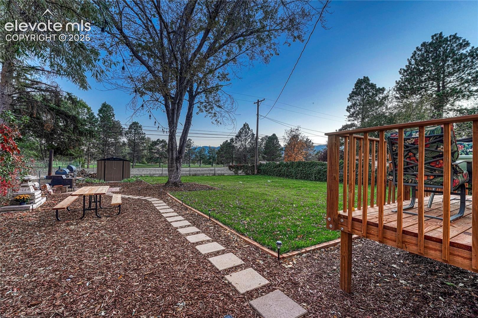 Rear yard featuring a raised wood deck, stone paver pathway, mature trees, and detached storage building