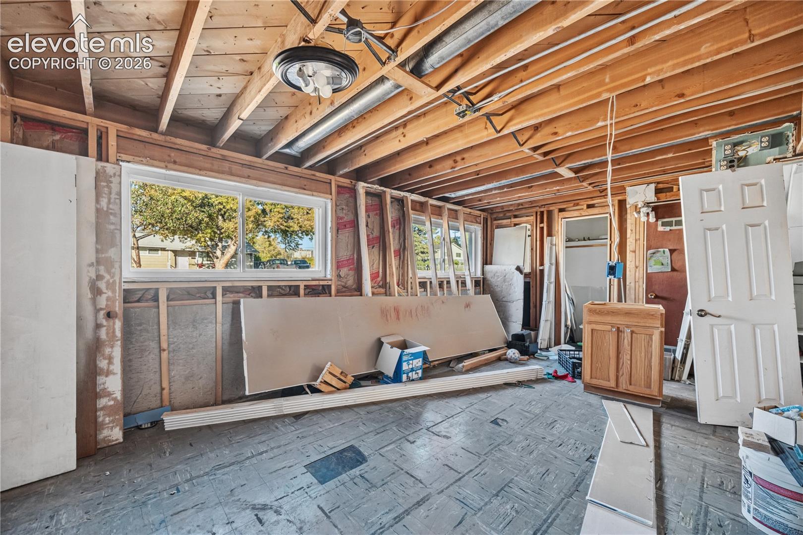 Exposed timber ceiling joists featuring dual sliding windows, an attached interior door, and a built-in wood-finish cabinet