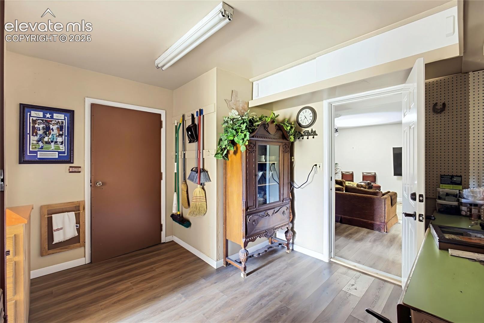 Wood-finish flooring, built-in wall-mounted pegboard storage, and linear overhead lighting
