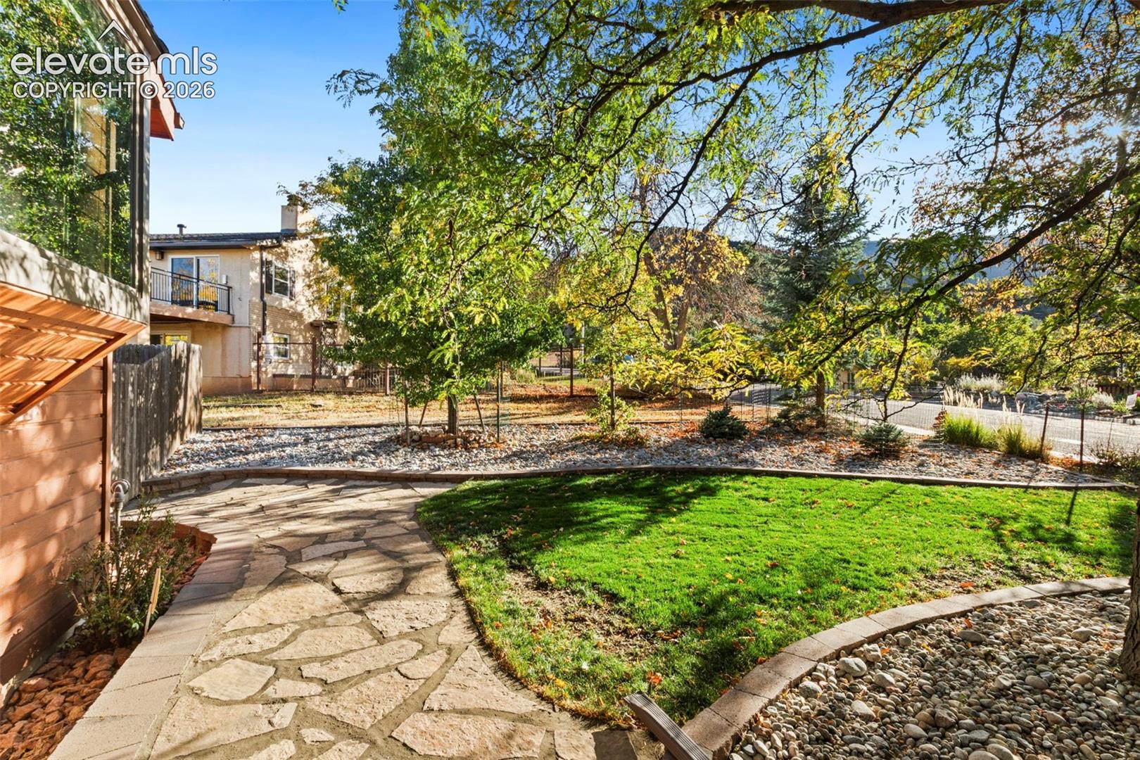 Flagstone patio featuring a grass lawn, decorative stone ground cover, and mature trees
