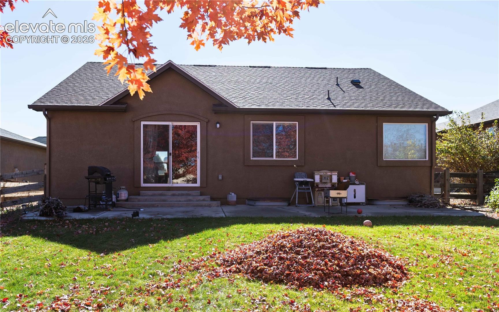 Stucco exterior featuring a concrete patio, sliding glass door, and asphalt shingle roof