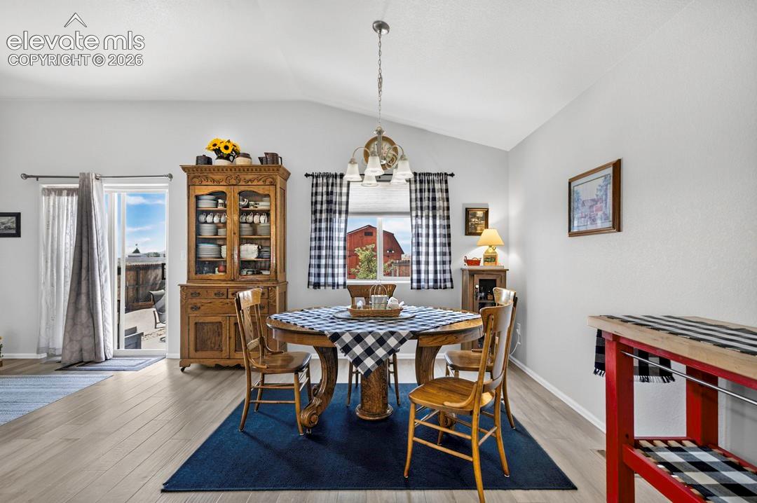 Vaulted ceilings enhance this dining area featuring wood-finish flooring, a contemporary ceiling light fixture, and a sliding glass door leading to the exterior patio