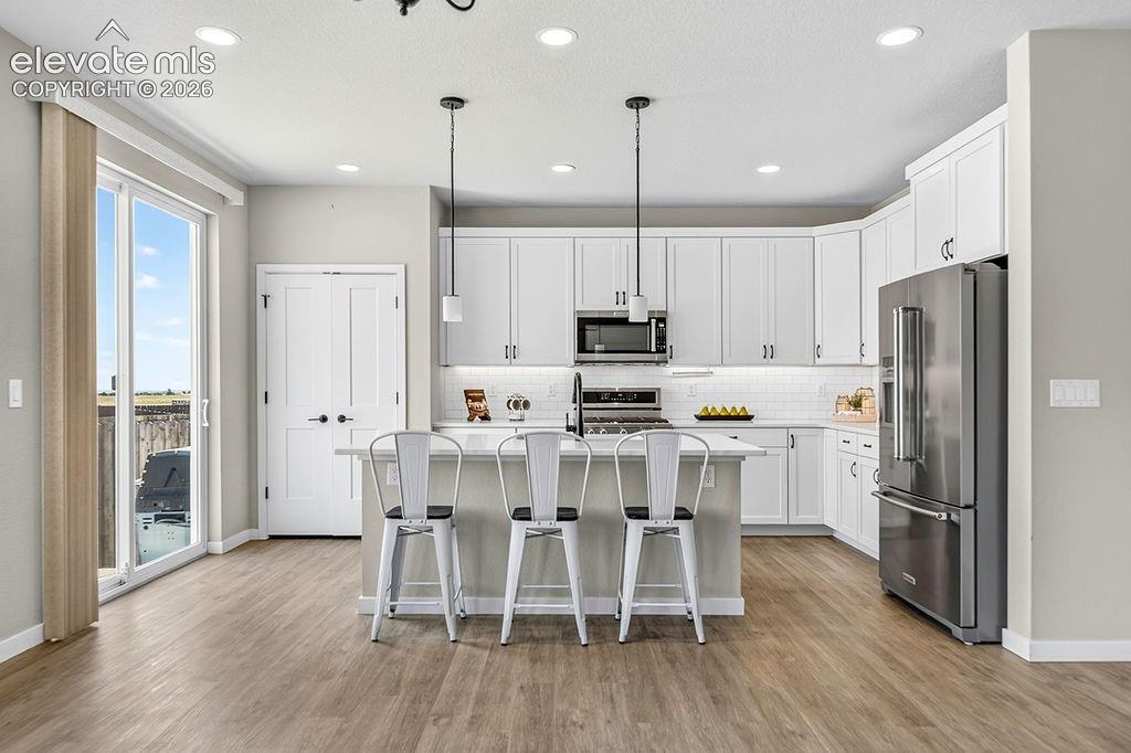 Kitchen featuring wood-finish flooring, white cabinetry with dark hardware, stainless steel appliances, a white subway tile backsplash, and a central island with pendant lighting