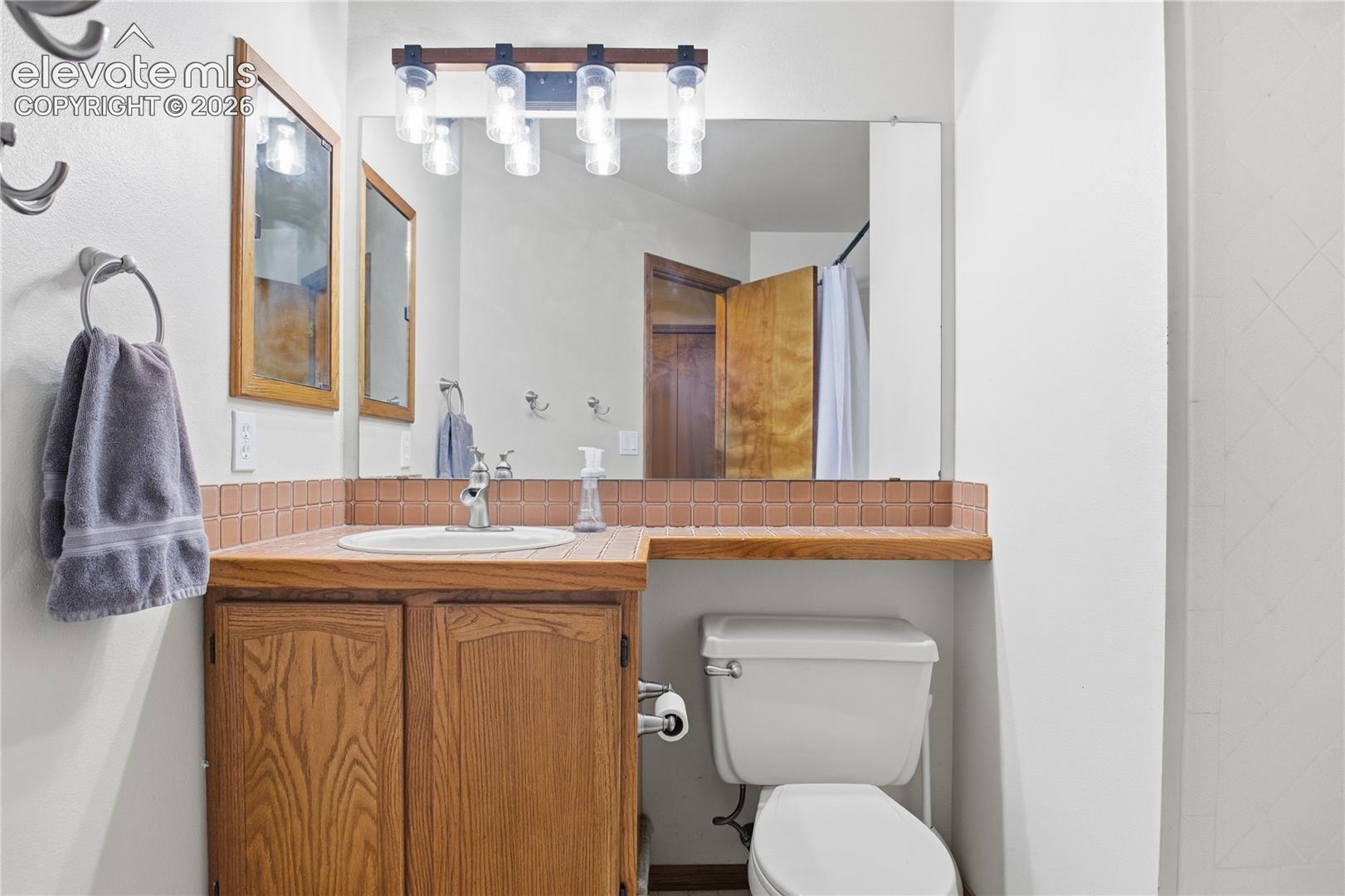 WOOD VANITY WITH A WOODEN COUNTERTOP, INSET SINK, TILE BACKSPLASH, AND OVERHEAD FOUR-LIGHT FIXTURE