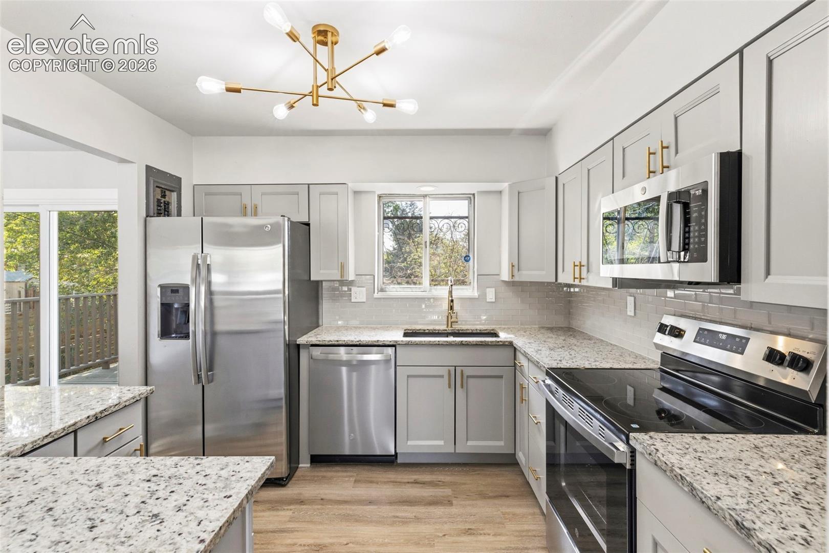 Kitchen featuring gray cabinetry with gold hardware, granite countertops, stainless steel appliances, and luxury vinyl plank flooring