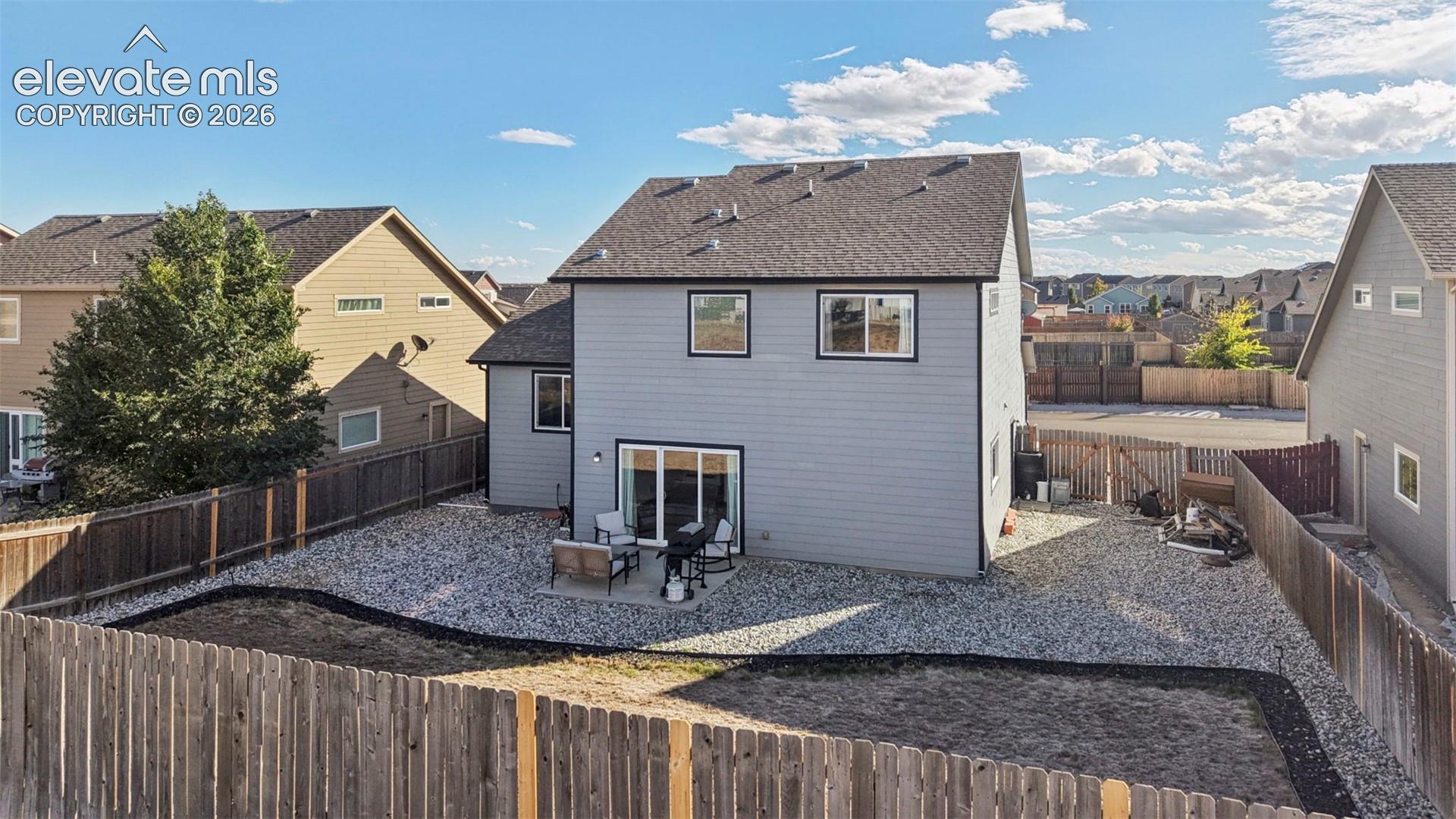 Two-story residence with horizontal siding, gable roof, sliding glass door, and fenced backyard featuring a stone-aggregate ground cover
