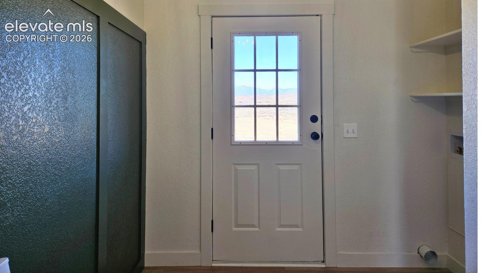 Exterior door with nine-lite window pane, paneled cabinetry, built-in shelving, and utility hookups