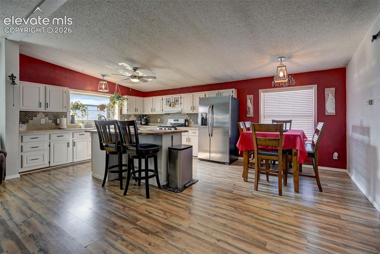 Kitchen with white cabinets, stainless steel appliances, a textured ceiling, light wood-style floors, and a breakfast bar area