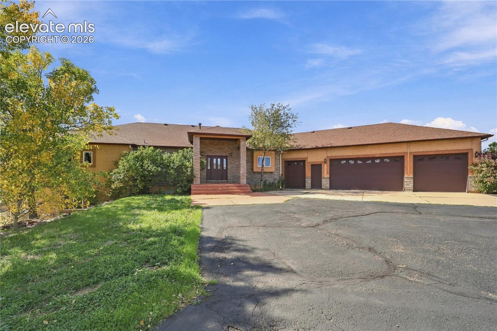 Stucco exterior with stone accents, multiple garage bays, covered entry, and a paved driveway