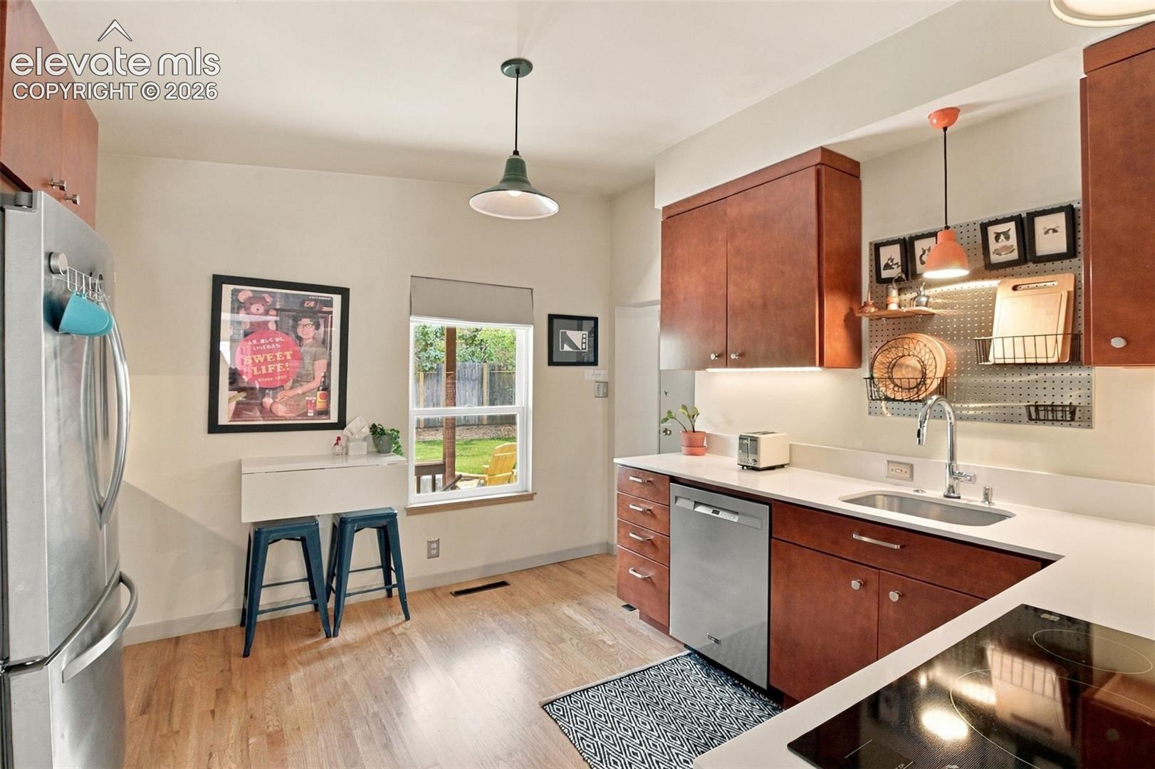 Kitchen featuring wood cabinetry, solid-surface countertops, stainless steel appliances, wood-finish flooring, and pendant lighting