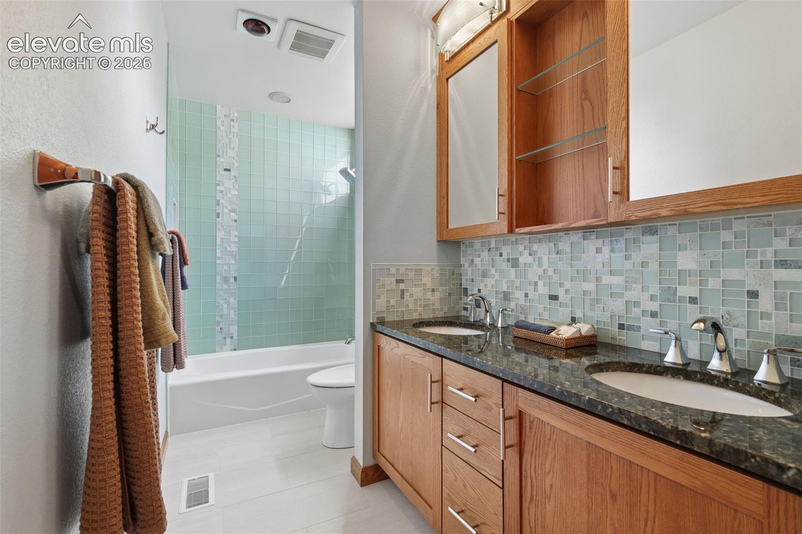 Remodeled bath featuring beautiful glass tile with granite counters, double sinks, and tile flooring.  Lots of extra storage in this bathroom.