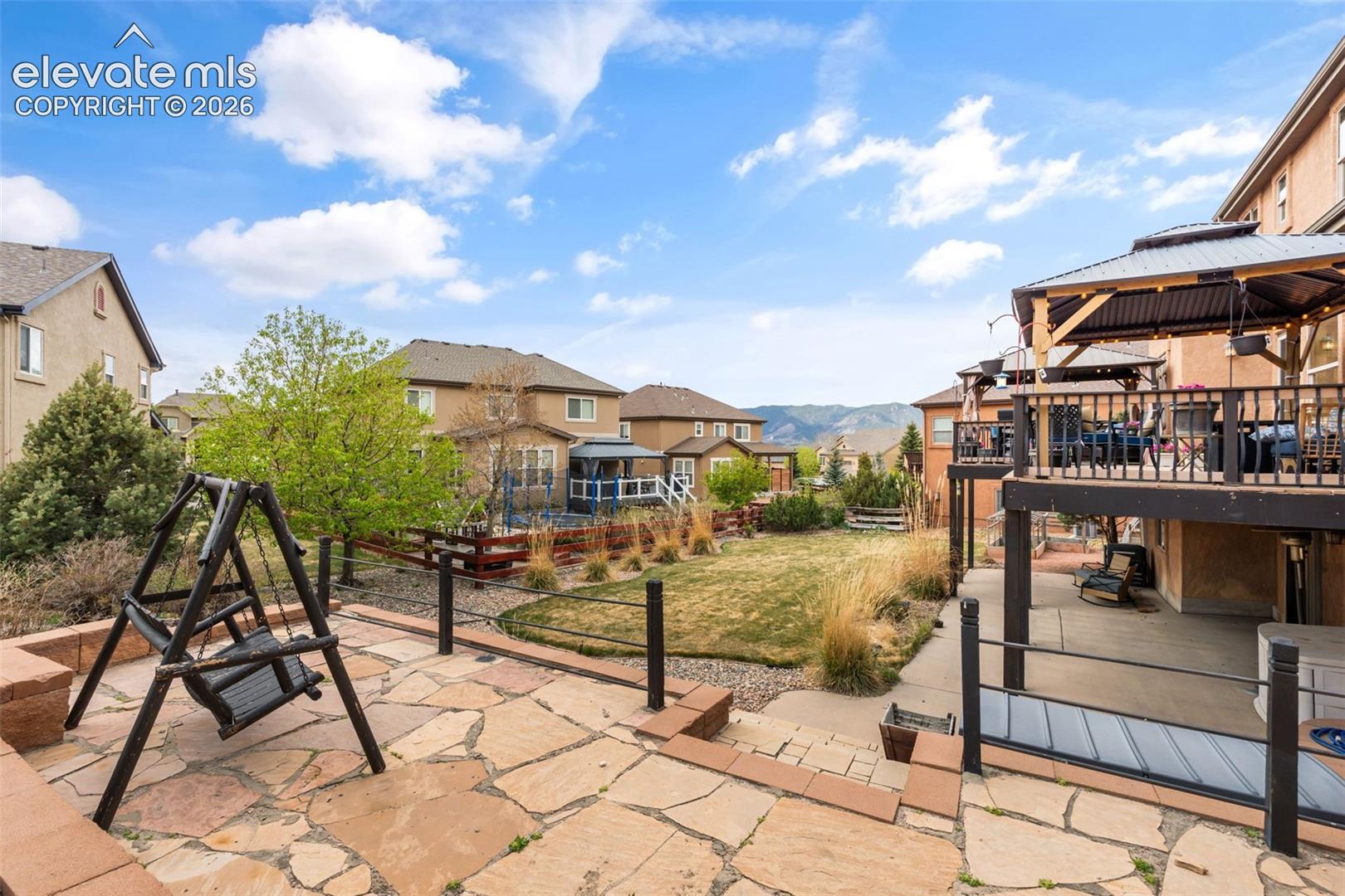 Multi-level outdoor living space featuring a spacious flagstone patio, an upper-level deck with a gazebo, a lower-level concrete patio, and a terraced lawn area