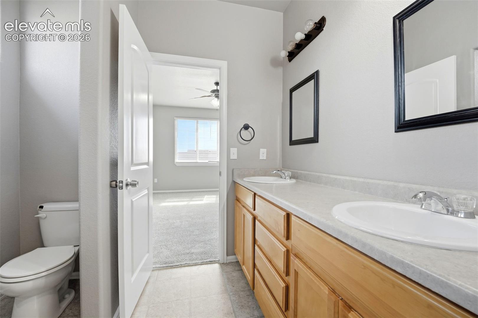 Dual sink vanity with light wood cabinetry, laminate countertop, and individual wall-mounted mirrors