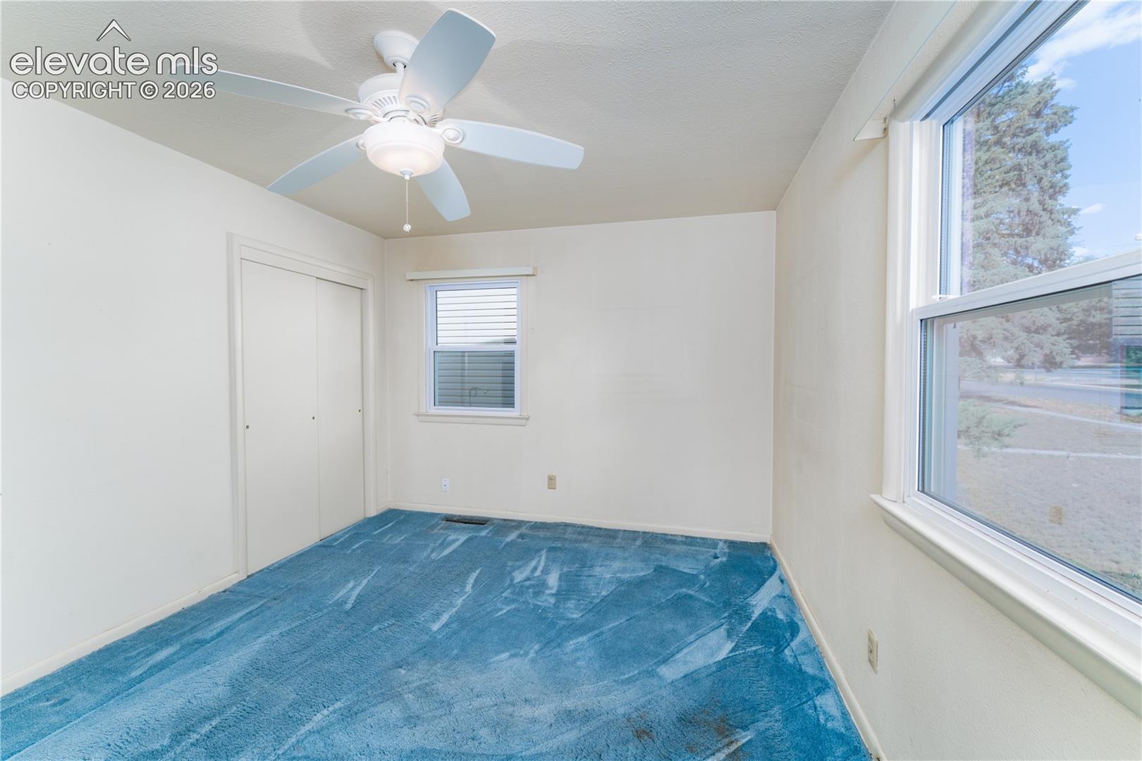 Room featuring a ceiling fan, two windows with white trim, and a built-in closet with sliding doors