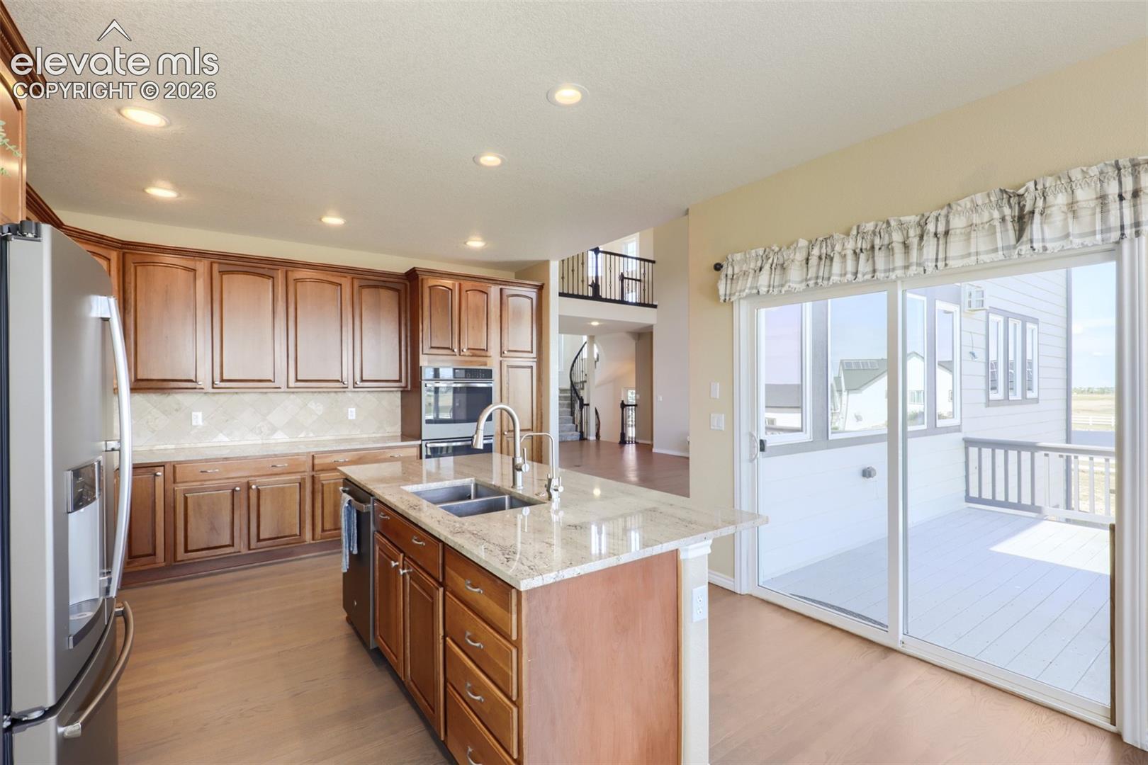Spacious, light-filled kitchen featuring solid wood cabinetry, granite countertops with a center island and breakfast bar, stainless steel appliances, recessed lighting, and hardwood flooring. The adjacent dining nook area opens directly through sliding glass doors onto an expansive back deck.