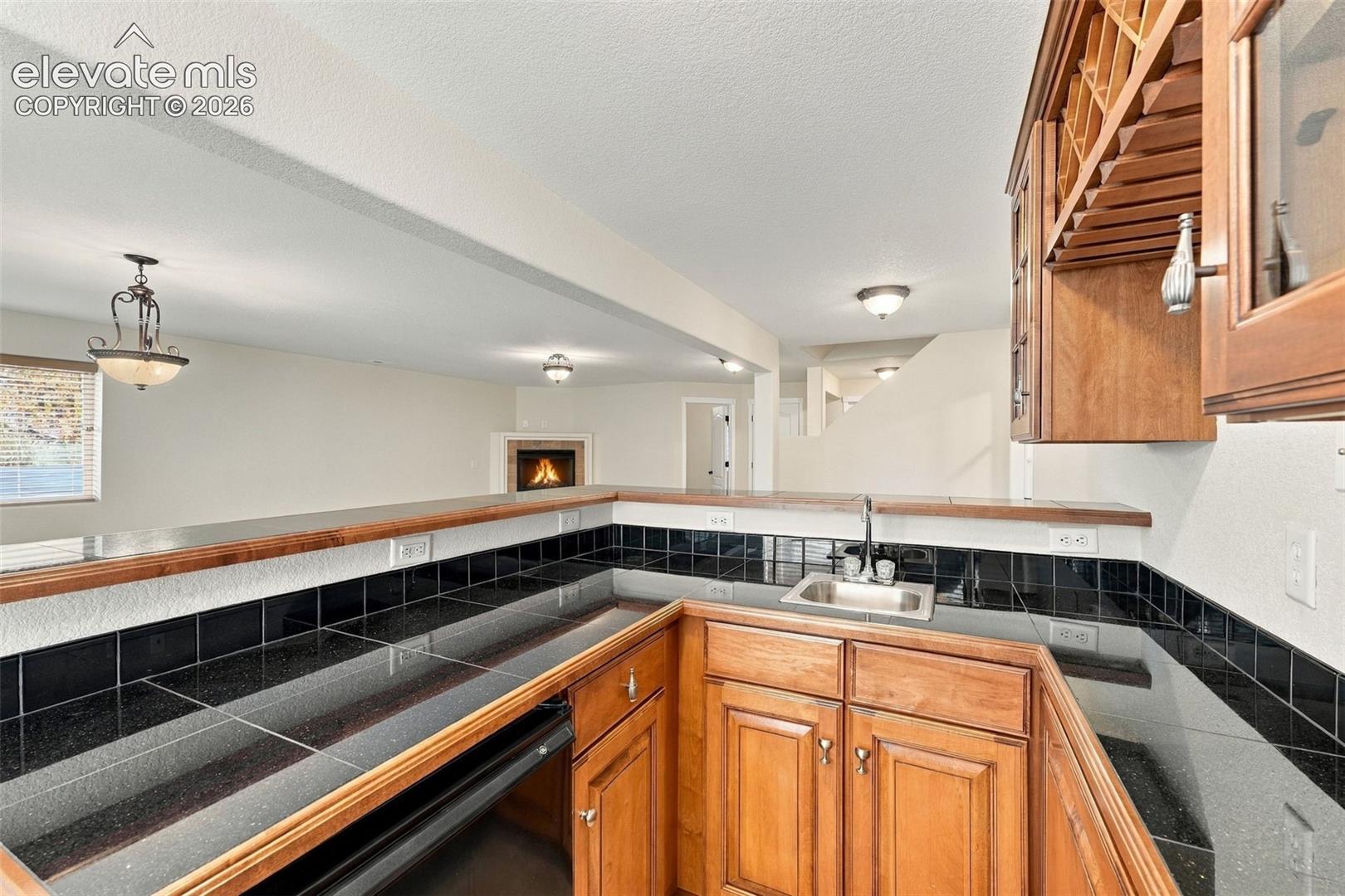 Kitchen featuring wood cabinetry, integrated wine storage, contrasting stone-finish countertops, black tile backsplash, and a drop-in stainless steel sink