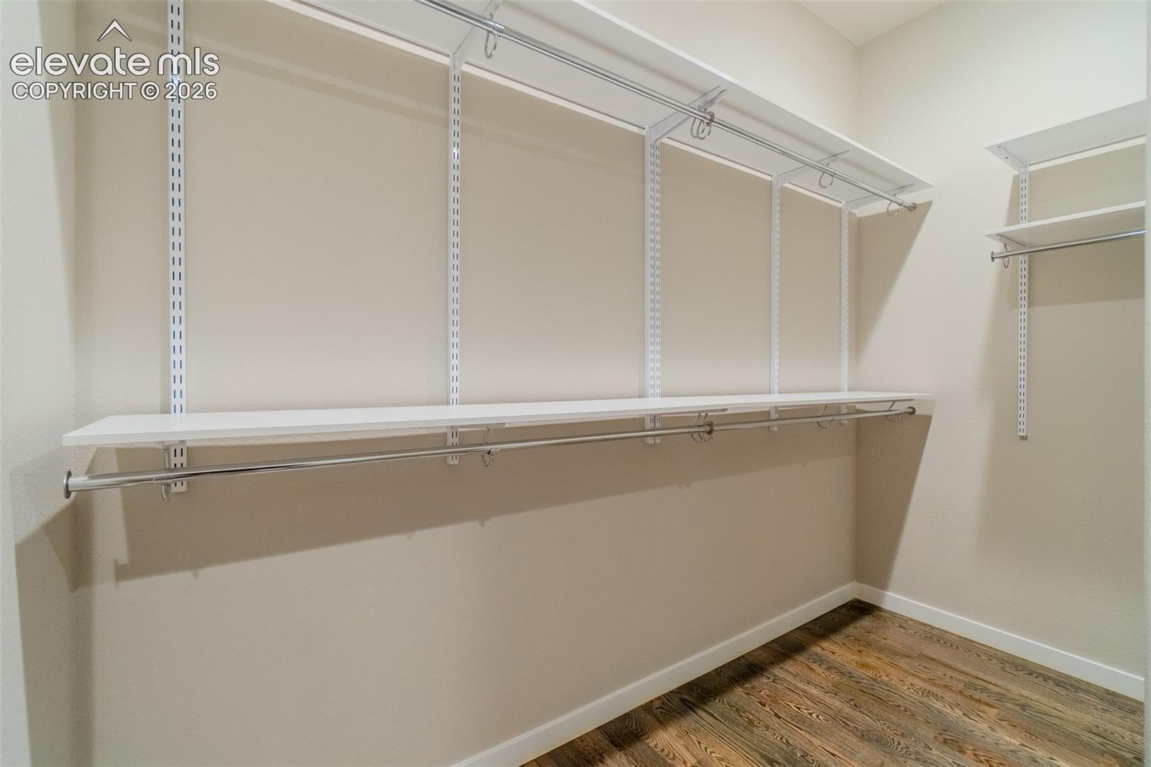 Closet featuring adjustable shelving, multiple hanging rods, and wood-finish flooring