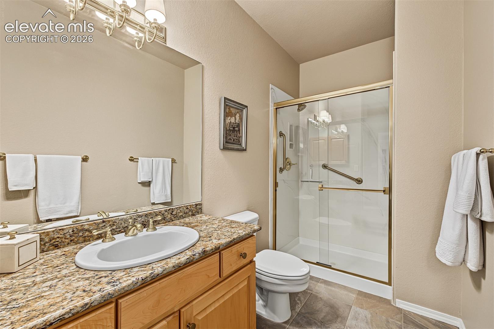Full bathroom adjoining the walkout basement bedroom suite, featuring a granite-topped vanity, tiled flooring, and a glass-enclosed shower.