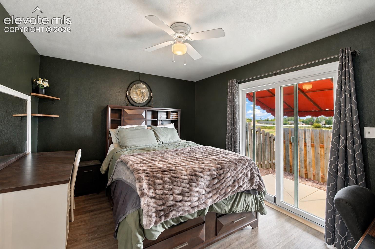 Sliding glass door to outdoor patio, wood-finish flooring, ceiling fan, and built-in headboard storage