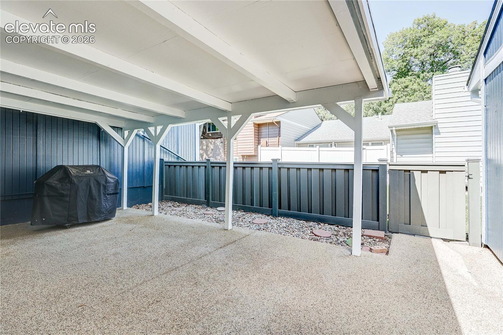 Covered patio with concrete flooring, supporting timber posts, and dark vertical exterior siding, complemented by a fenced perimeter and integrated gate