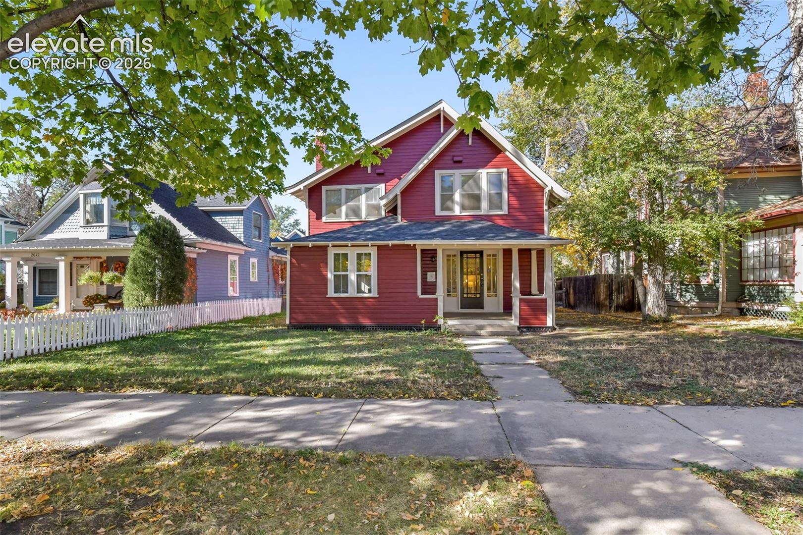 Two-story exterior featuring deep red siding, a covered front porch, multi-pane windows, a peaked roofline, and a concrete walkway