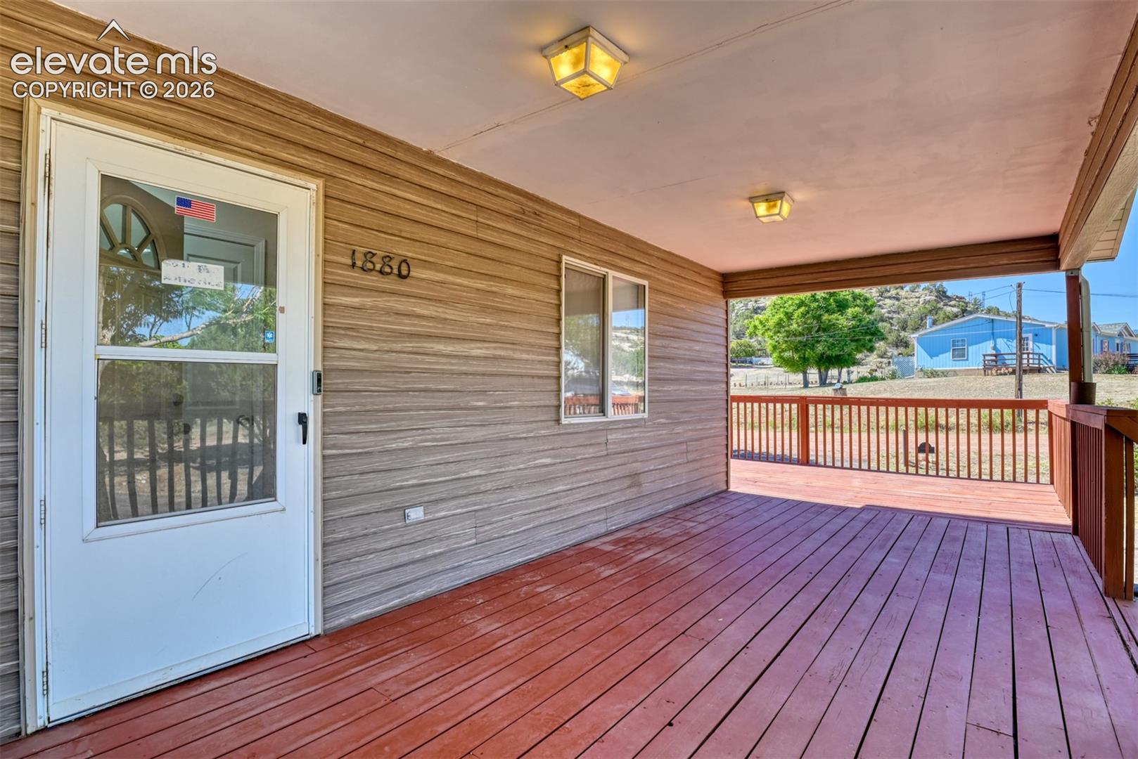 Covered front porch with wood-finish decking, horizontal siding, and flush-mounted ceiling lighting