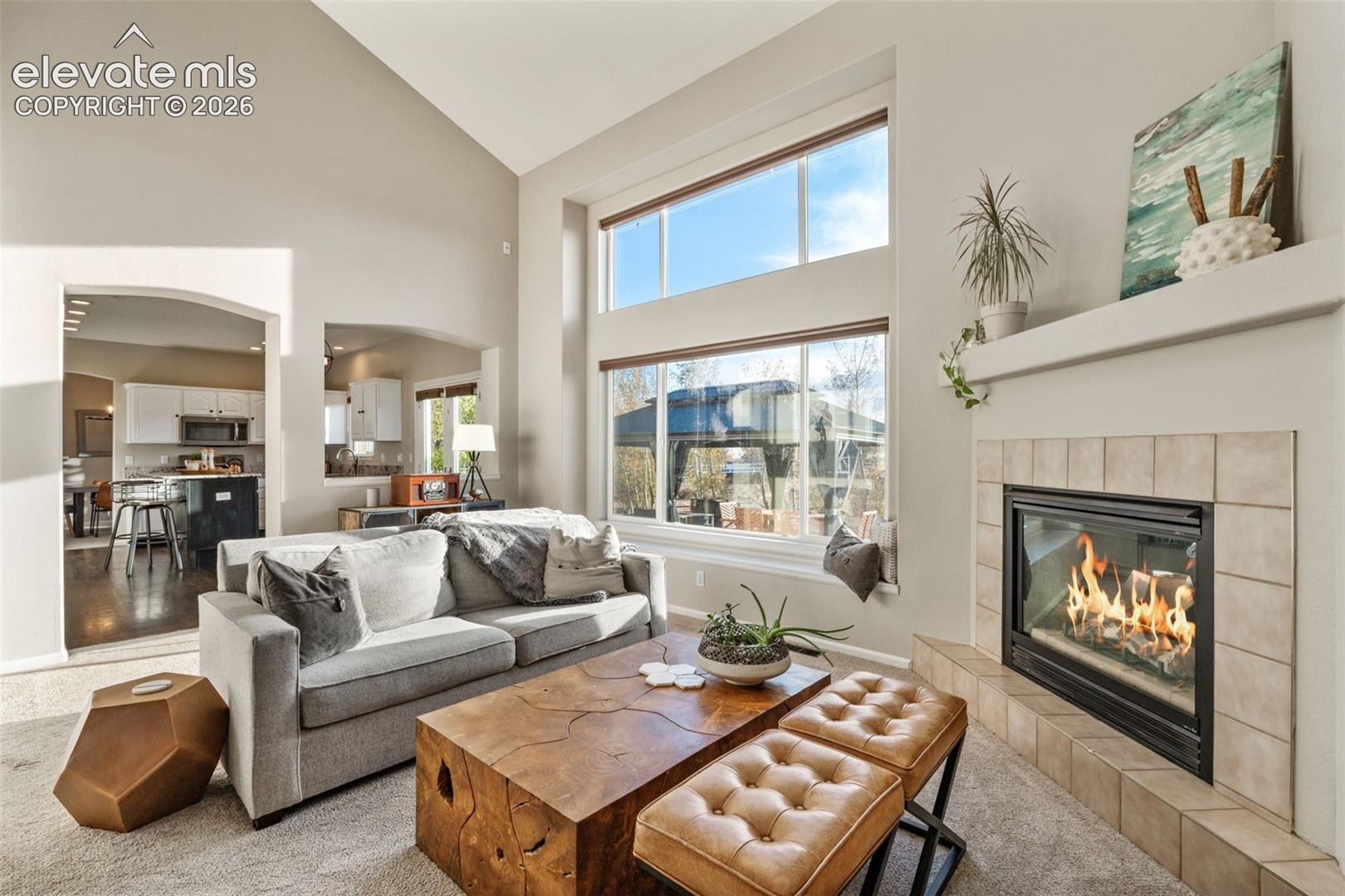 Vaulted ceilings, large-scale windows with multi-pane configuration, and a fireplace featuring a tile surround and mantel