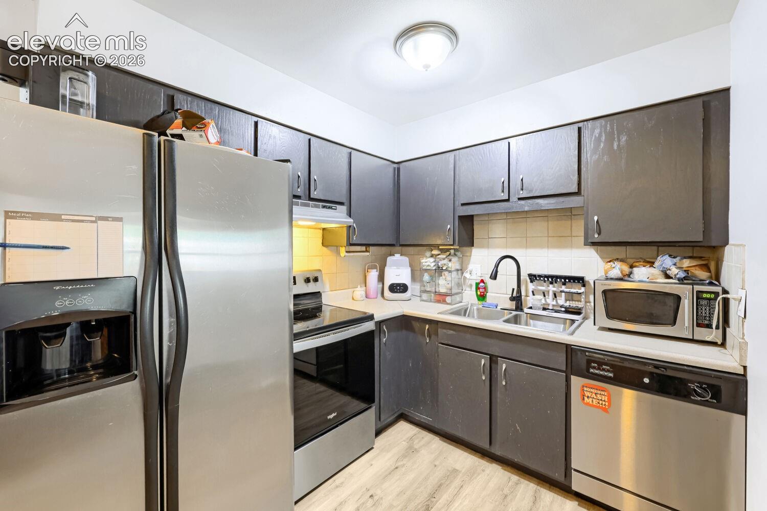 Kitchen featuring stainless steel appliances, dark cabinetry, light-toned countertops, and wood-finish flooring