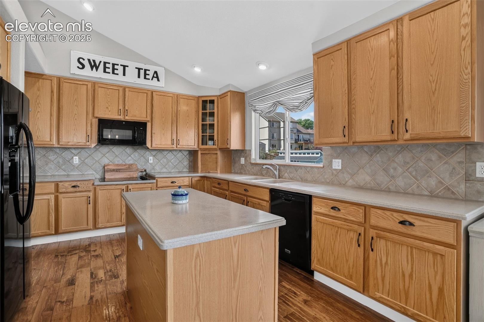 Kitchen featuring wood-finish flooring, light wood cabinetry, light-toned countertops, and a tile backsplash