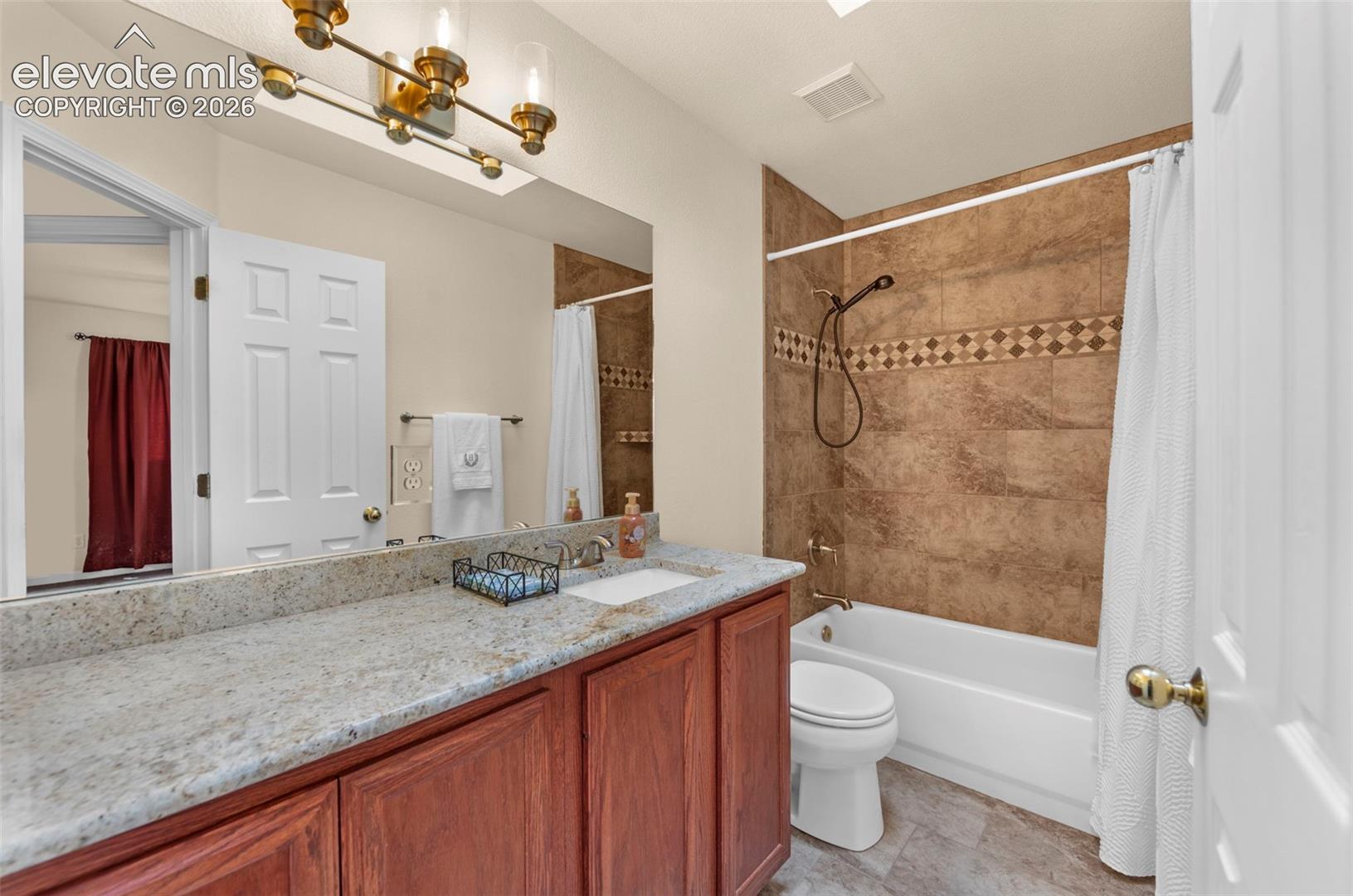 Bathroom featuring a wood-finish vanity with a light speckled countertop, single basin sink, and a large wall-mounted mirror