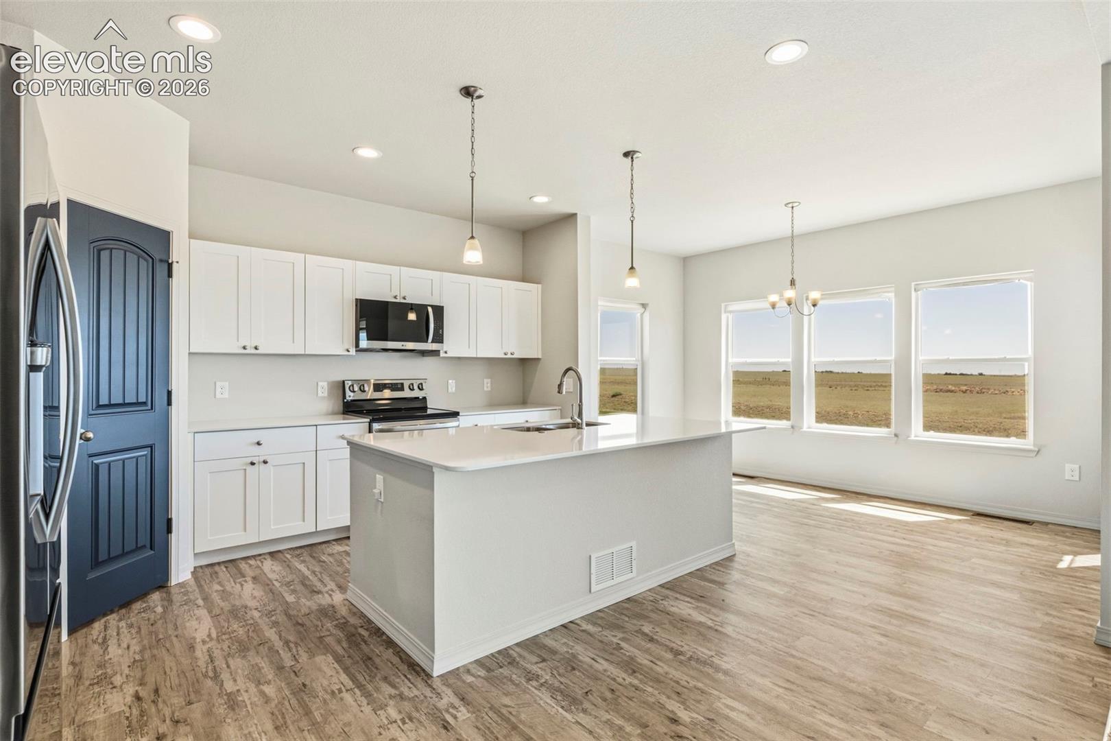 Open-concept kitchen featuring white shaker cabinetry, an island with an undermount sink, stainless steel appliances, and recessed lighting