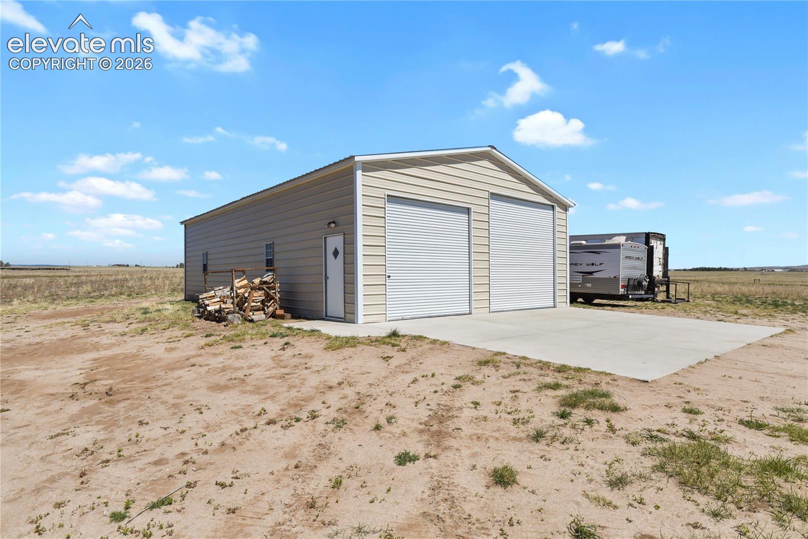 Detached metal-sided structure featuring dual roll-up garage doors, a pedestrian door, and a concrete apron