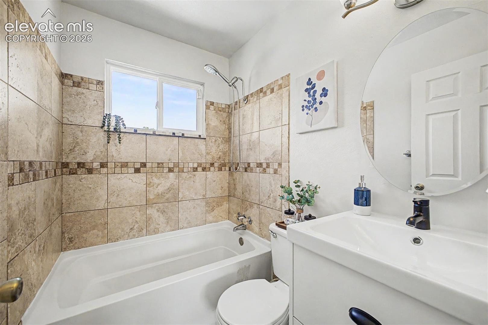 Bathroom featuring a tiled shower surround with decorative accent band, a built-in bathtub, and a window to let the light in. 
