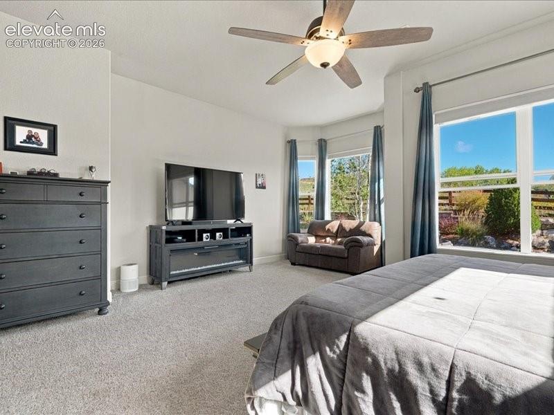 Bay window offering natural light, ceiling fan with integrated lighting, recessed wall-mounted electric fireplace, and light-colored carpeting
