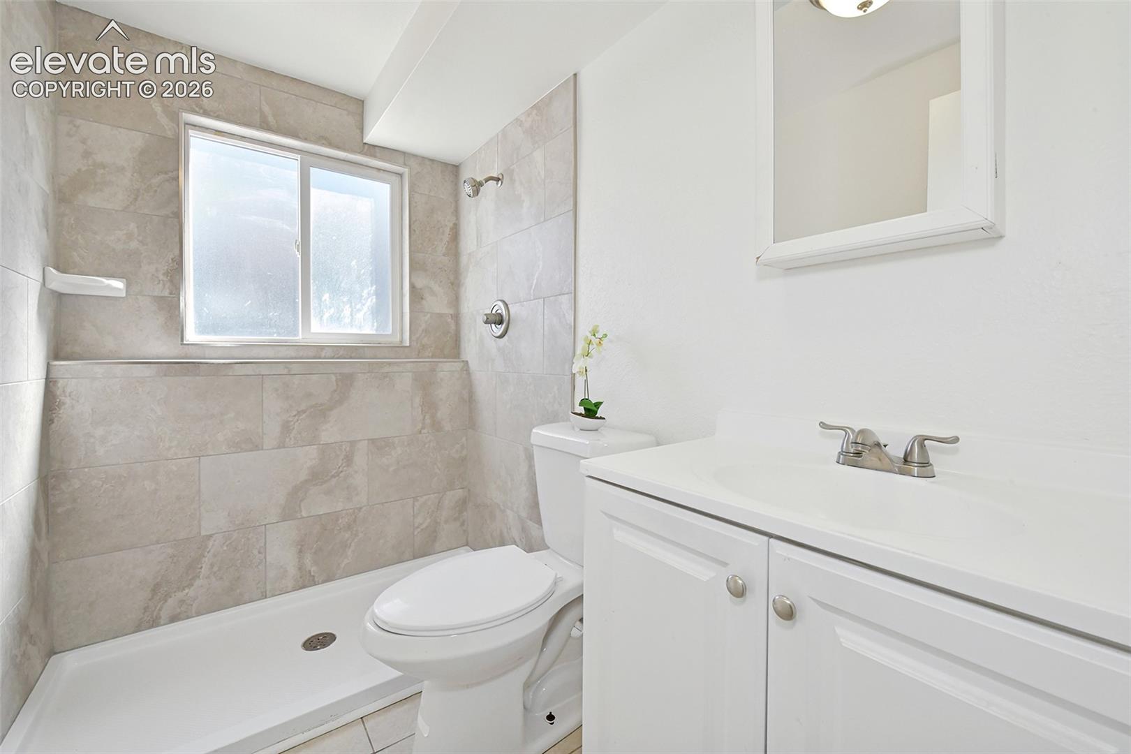 Bathroom featuring a walk-in shower with stone-finish tile surround, white vanity cabinet 
