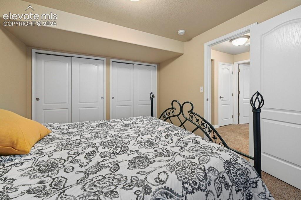 Basement bedroom with Ornamental Metal Bed Frame, Patterned Bedding, Dual Closets with White Panel Doors, Attached Ensuite Access, and Neutral Carpeting Throughout