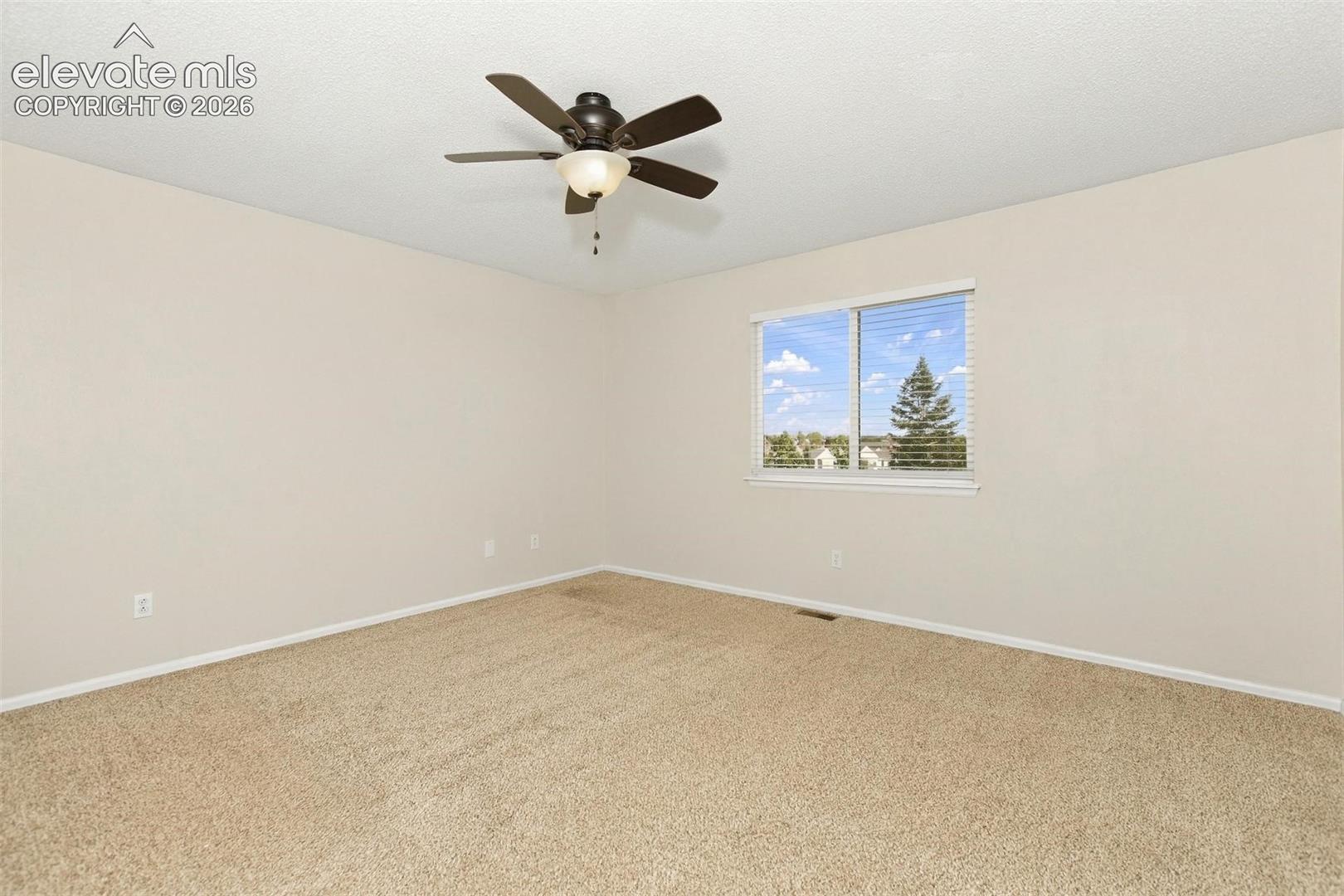 Neutral-toned carpeted room featuring a ceiling fan with integrated lighting and a window with exterior scenery