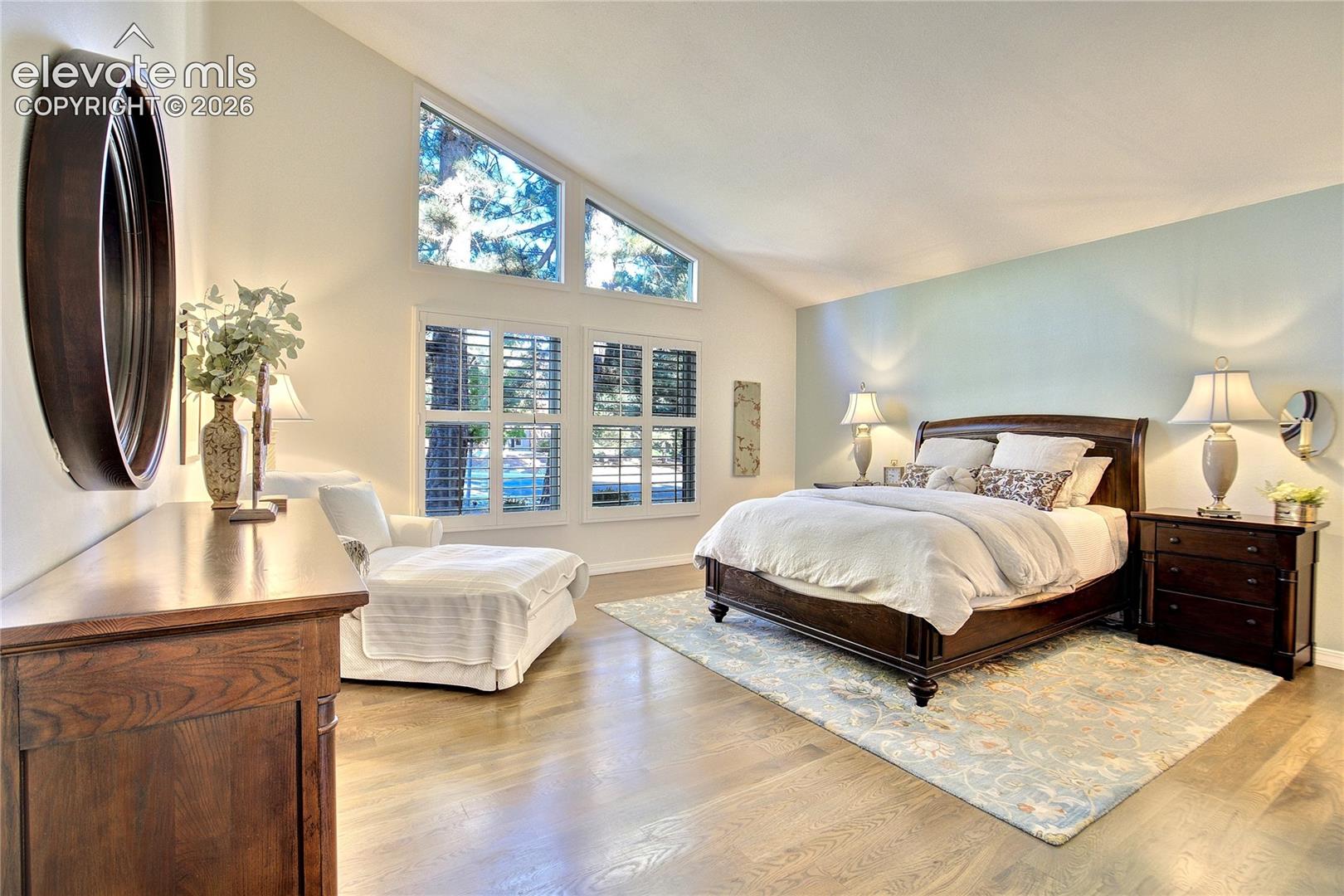 The main-level primary suite pairs dramatic vaulted ceilings, gleaming hardwoods + generous proportions.